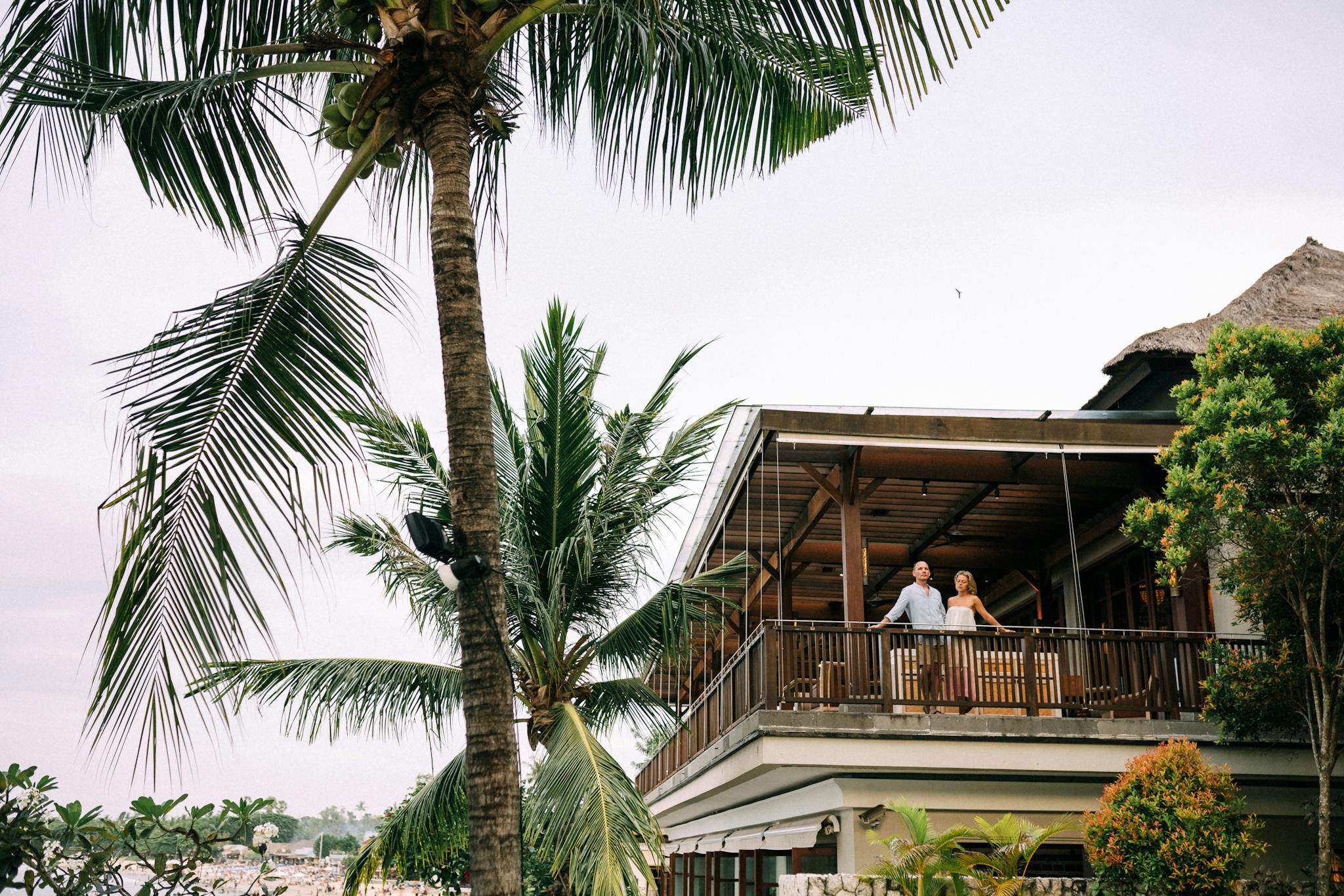 A couple enjoys a peaceful moment on a luxury resort balcony surrounded by palm trees.