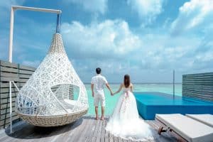 A newlywed couple holding hands, enjoying a seaside resort with infinity pool.