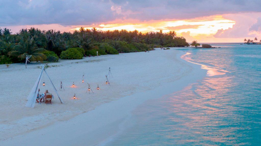A romantic beach setting with lights and seating at sunset in the Maldives.