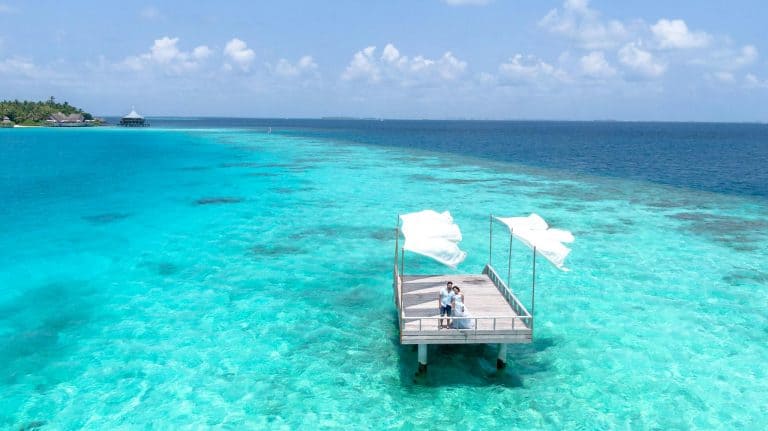 Aerial view of a couple on a deck above the turquoise waters of the Maldives, capturing a romantic moment.