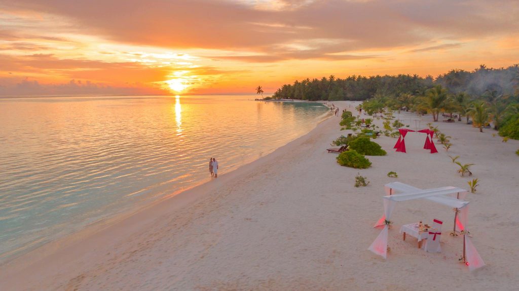 Couple enjoys a romantic walk on a serene Maldivian beach during a breathtaking sunset.