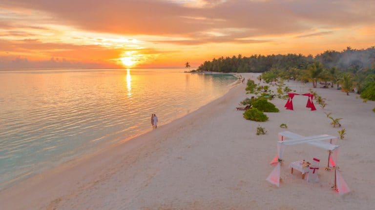 Couple enjoys a romantic walk on a serene Maldivian beach during a breathtaking sunset.