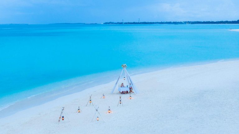 Drone view of a romantic beach dinner setup by the turquoise waters of the Maldives.