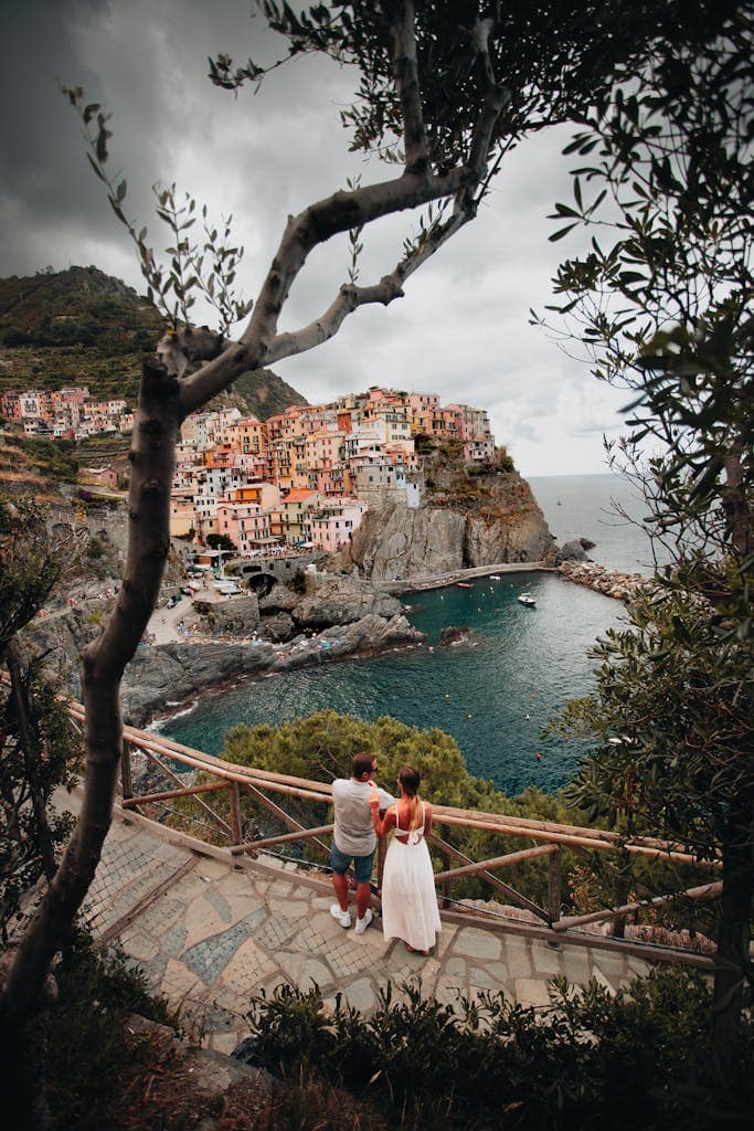 A couple stands on a scenic overlook, gazing at the colorful coastal village of Cinque Terre, Italy.