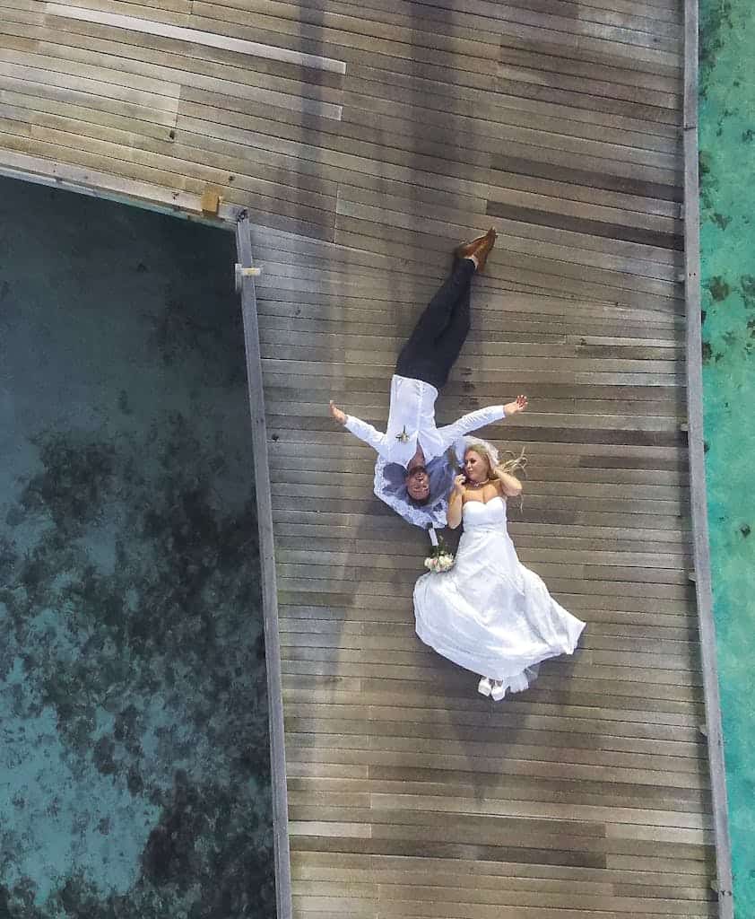 Aerial view of a bride and groom relaxing on a wooden pier over turquoise waters in the Maldives.