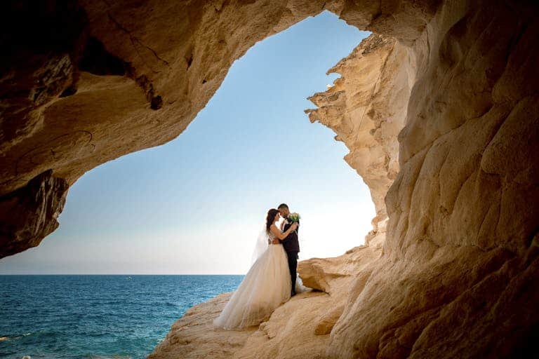 Bride and groom embracing in a rocky coastal setting, celebrating their wedding day with a scenic backdrop.